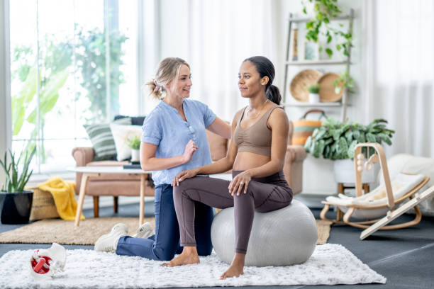 A professional helping a pregnant woman do physiotherapy exercising with a pelvic floor personalized treatment plan on a ball.