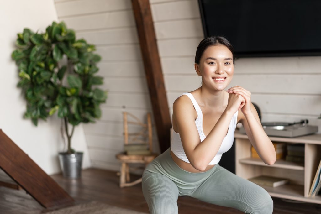 An Asian woman smiling and doing squats.